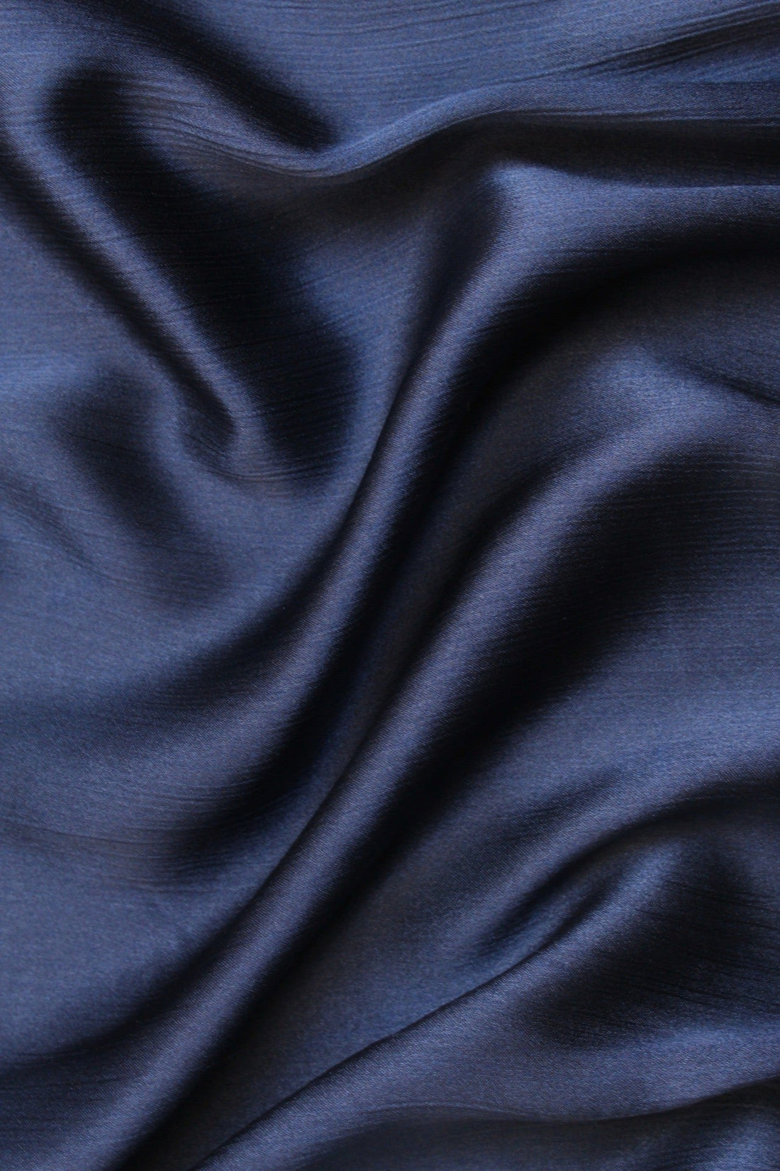 A navy blue silk hijab with a crinkled texture on one side and a matte finish on the other, providing a non-slip fit.