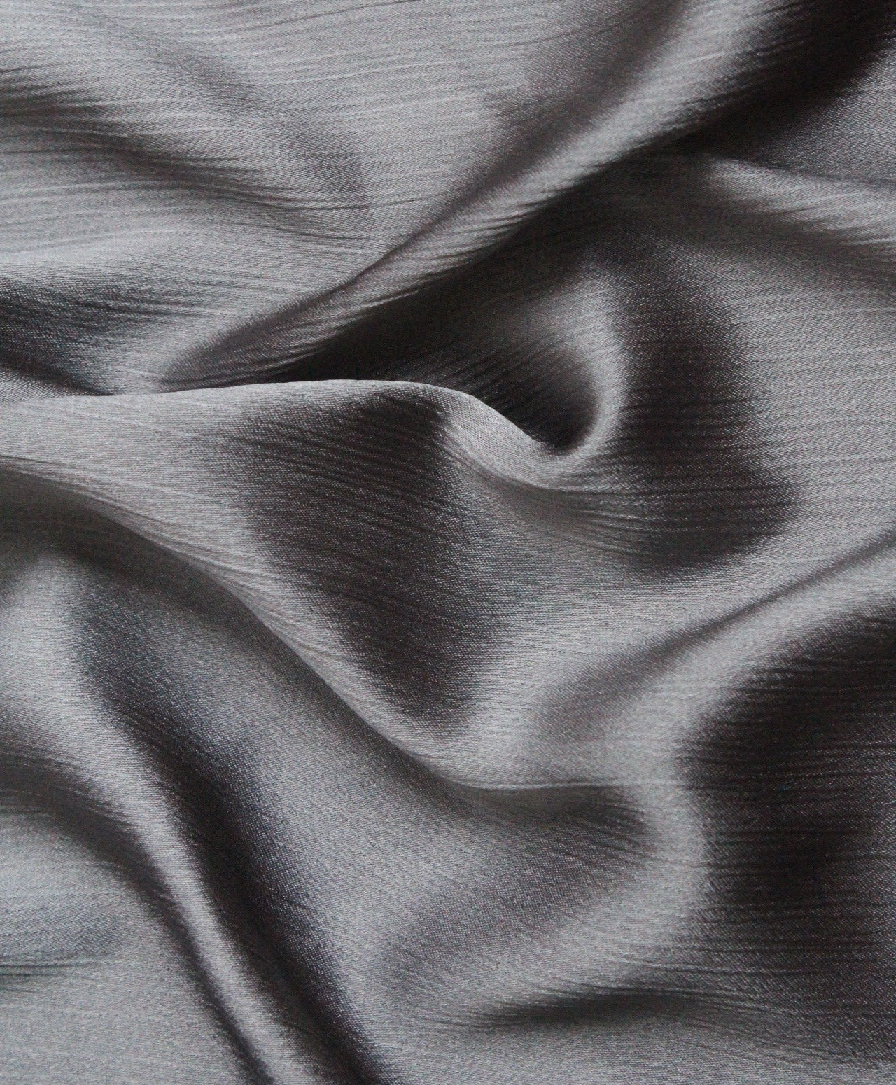 A luxurious silk hijab in a smoke gray color, showing a crinkled texture on one side and a matte finish on the other, highlighting its dual-texture design.