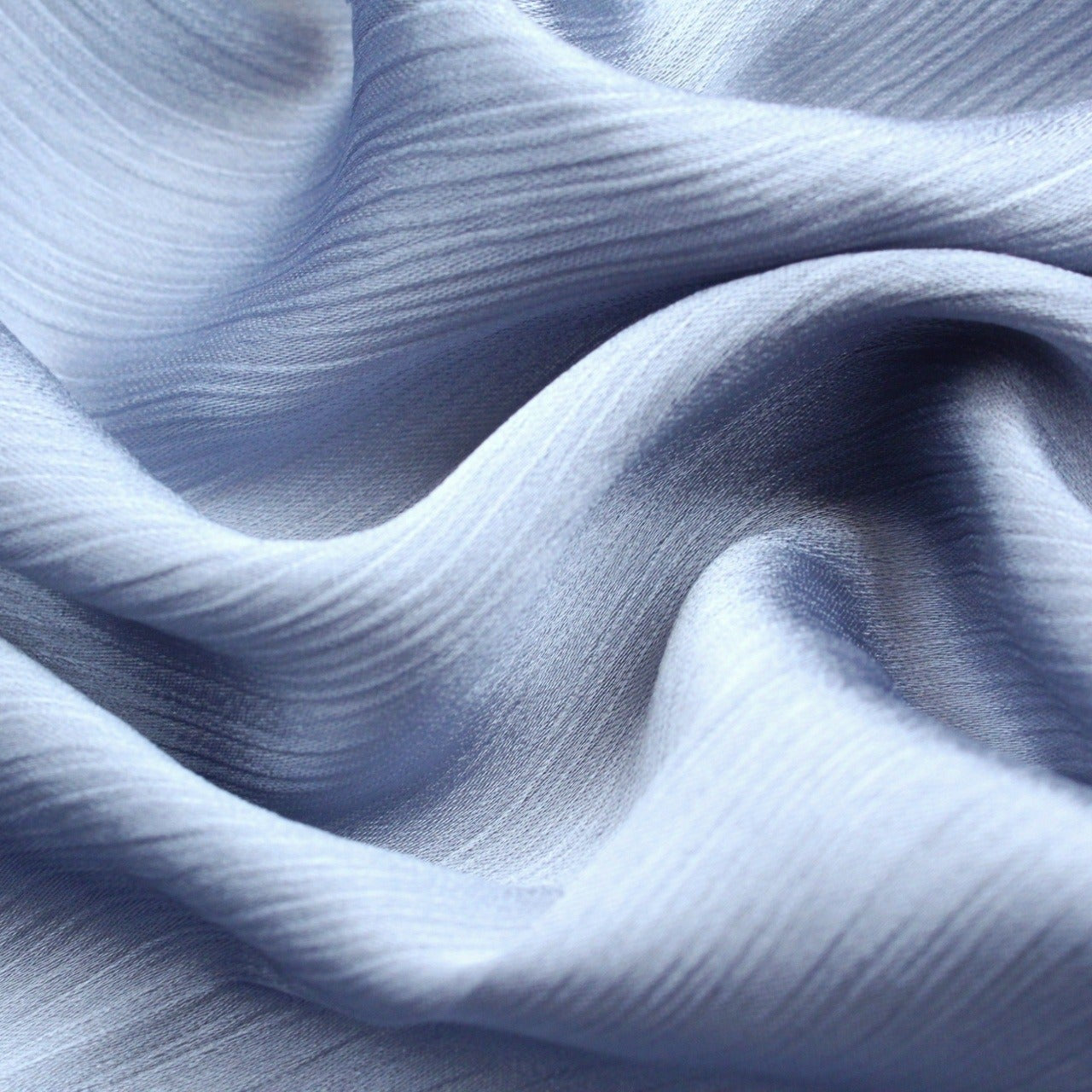 A close-up image of a baby blue silk hijab with a crinkled texture on one side and a matte finish on the other, highlighting its dual-texture design.