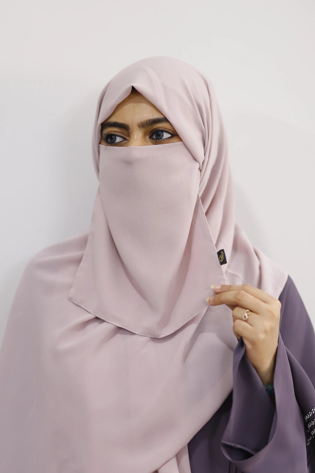 Person wearing a light pink hijab and purple garment on a white background